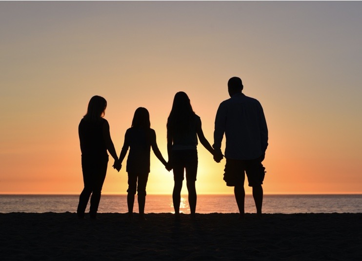 Family standing on a beach.  Head of household, married with children.